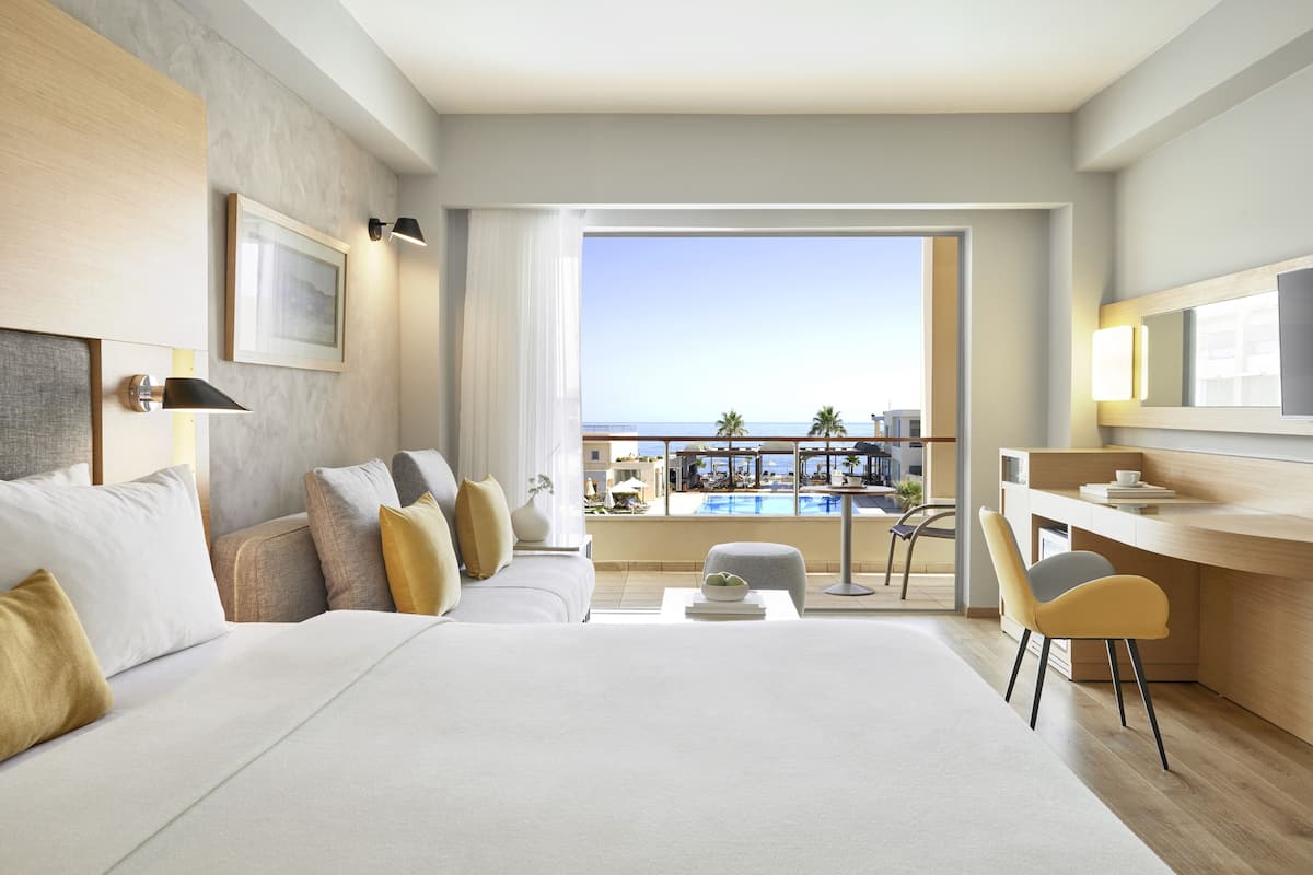 A hotel room with a large bed, a desk, and a view of a pool and buildings.
