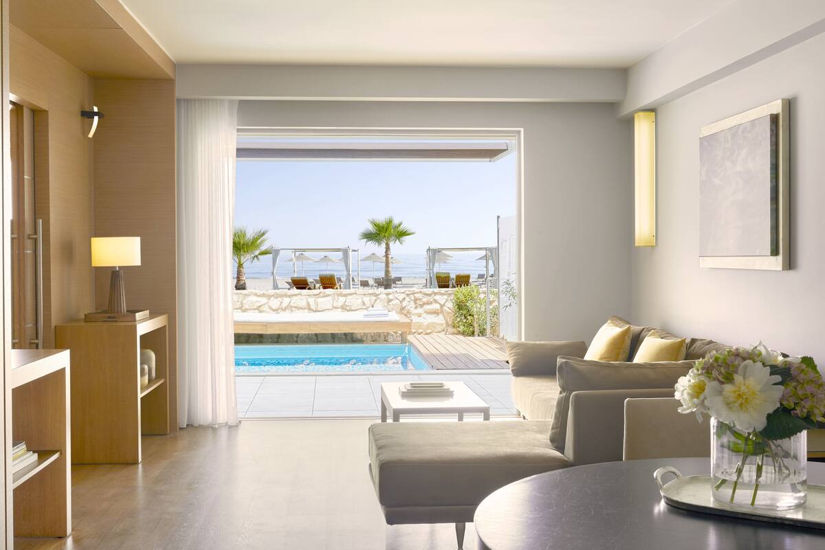 A modern living room with a pool view, a sofa, a coffee table, and a vase with flowers.