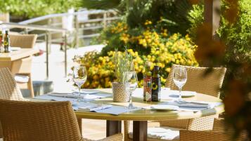 An outdoor dining area with wicker chairs and tables, a potted plant, and a bottle of olive oil.