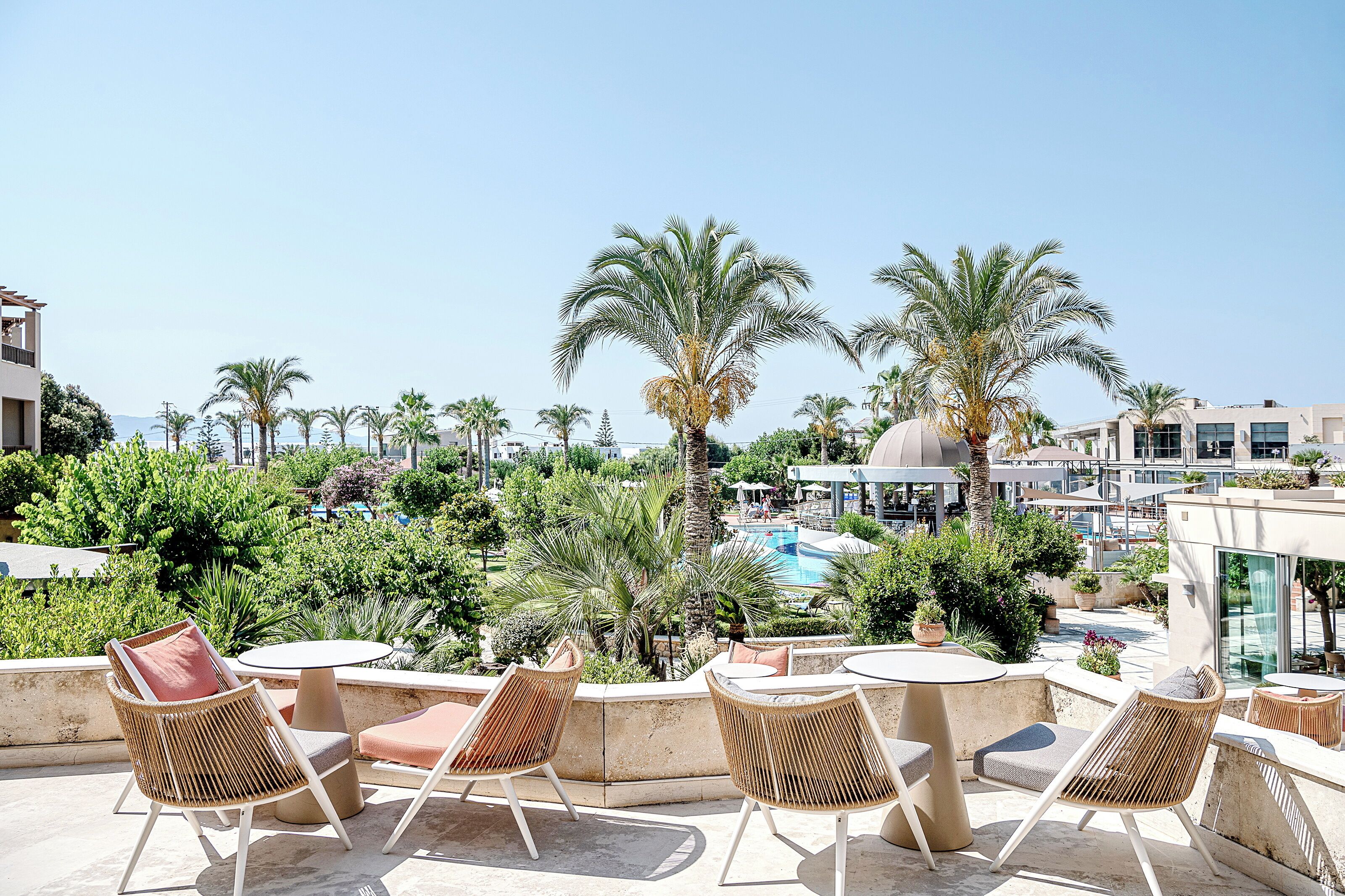 Una terraza en la azotea con mobiliario de mimbre, una piscina y palmeras.