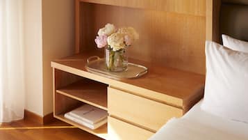 Ein ordentlich eingerichtetes Hotelzimmer mit einem Nachttisch aus Holz, einer Vase mit Blumen, einem Tablett und einem Buch mit dem Titel „ART NOUVEAU“.