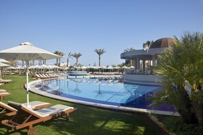 A pool area with lounge chairs and umbrellas, surrounded by palm trees and a clear sky.
