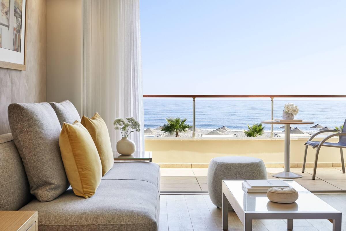 A balcony with a sofa, a table, and a view of the sea.
