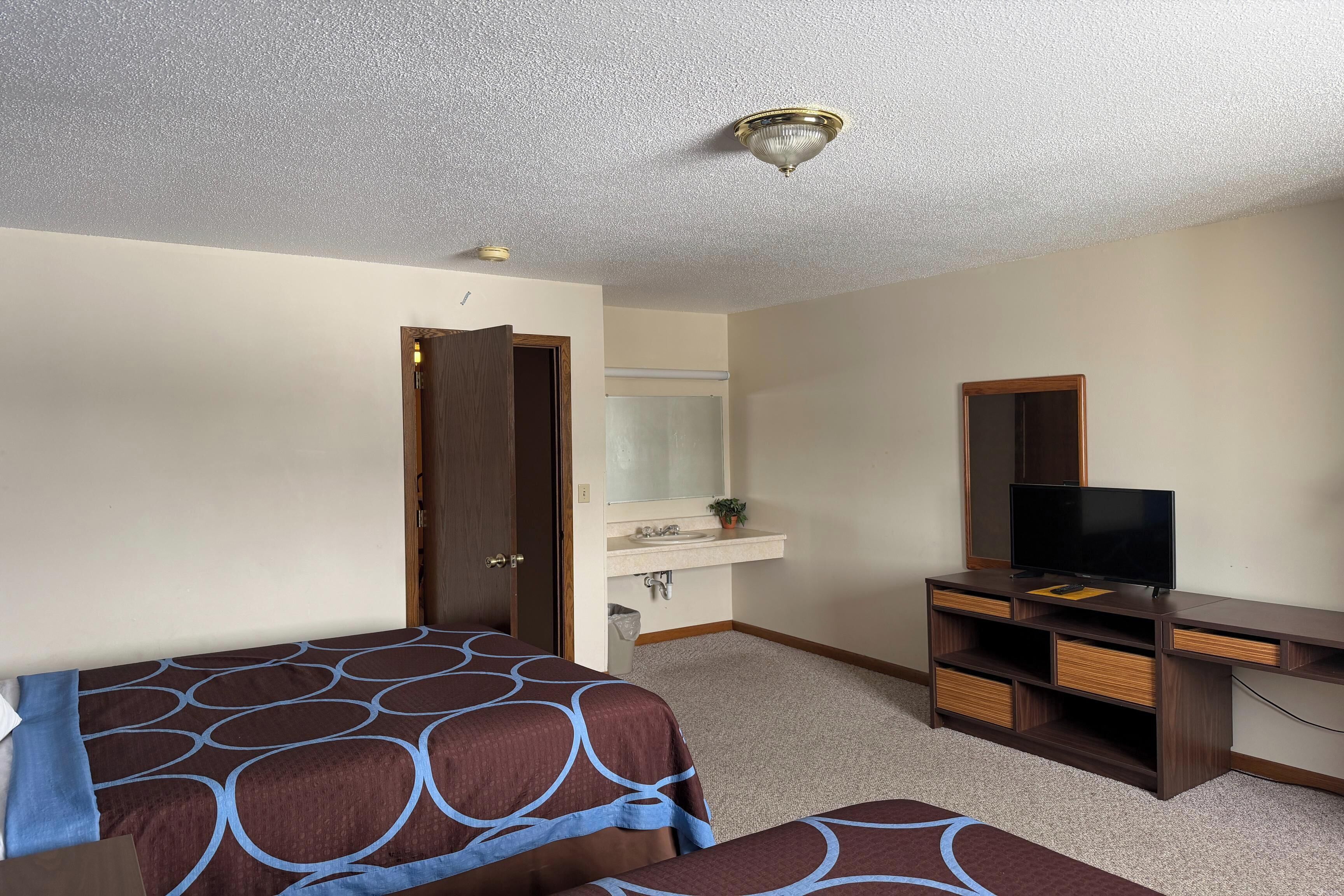 Habitación de hotel con dos camas, televisión, escritorio, espejo y baño.