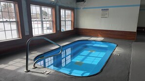 A swimming pool with a metal ladder, large windows, and a caution sign on the wall. - Iron Mountain Inn & Suites MI US 2 (Iron Mountain)