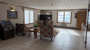 A living room with a television, two armchairs, a coffee table, and a bookshelf. - Iron Mountain Inn & Suites MI US 2 (Iron Mountain)