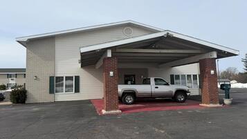 A building with a covered parking area, a brick pillar, and a white pickup truck parked under the shelter.