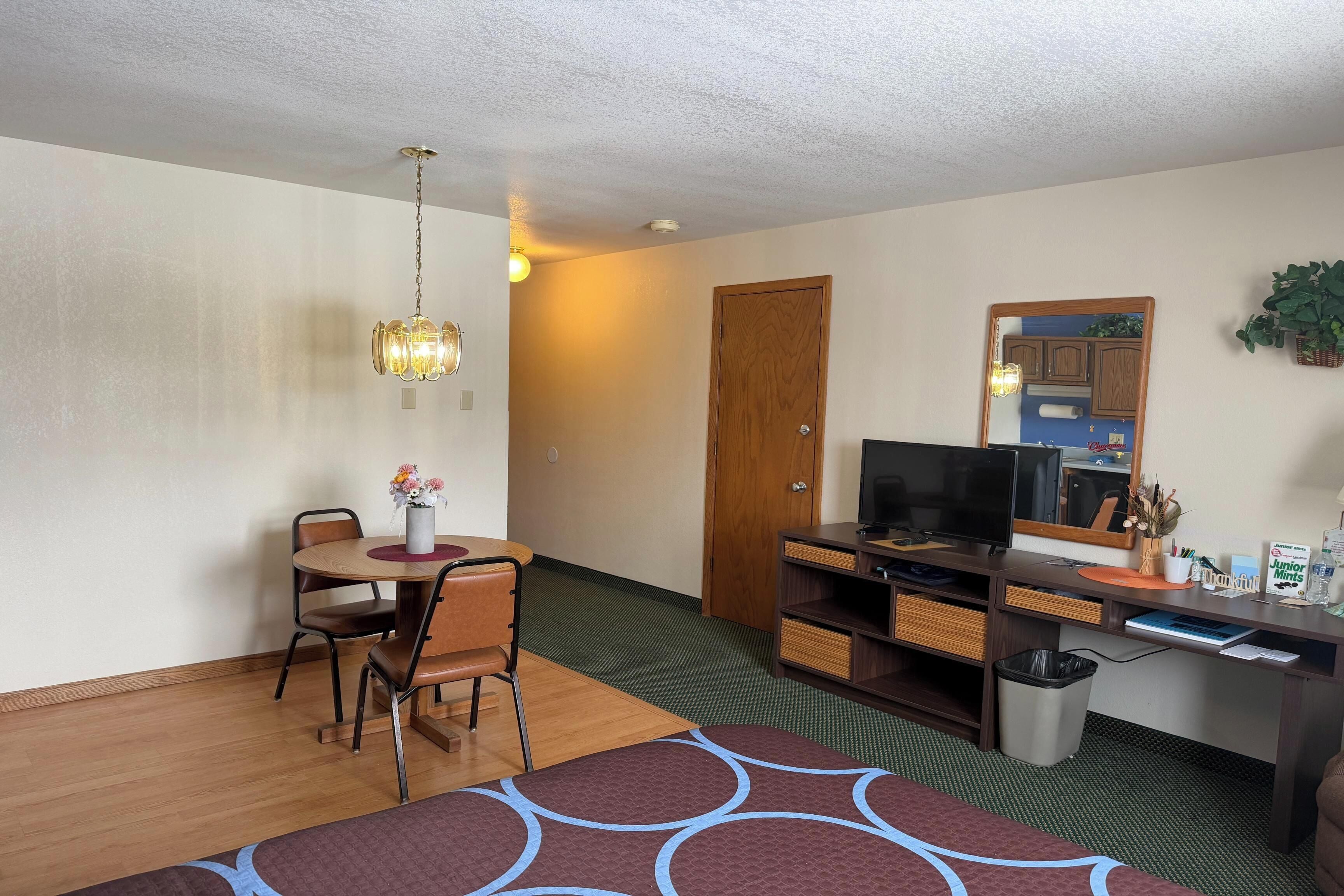 Ein Zimmer mit Esstisch, Stühlen, Fernseher, Schreibtisch und Mülleimer.