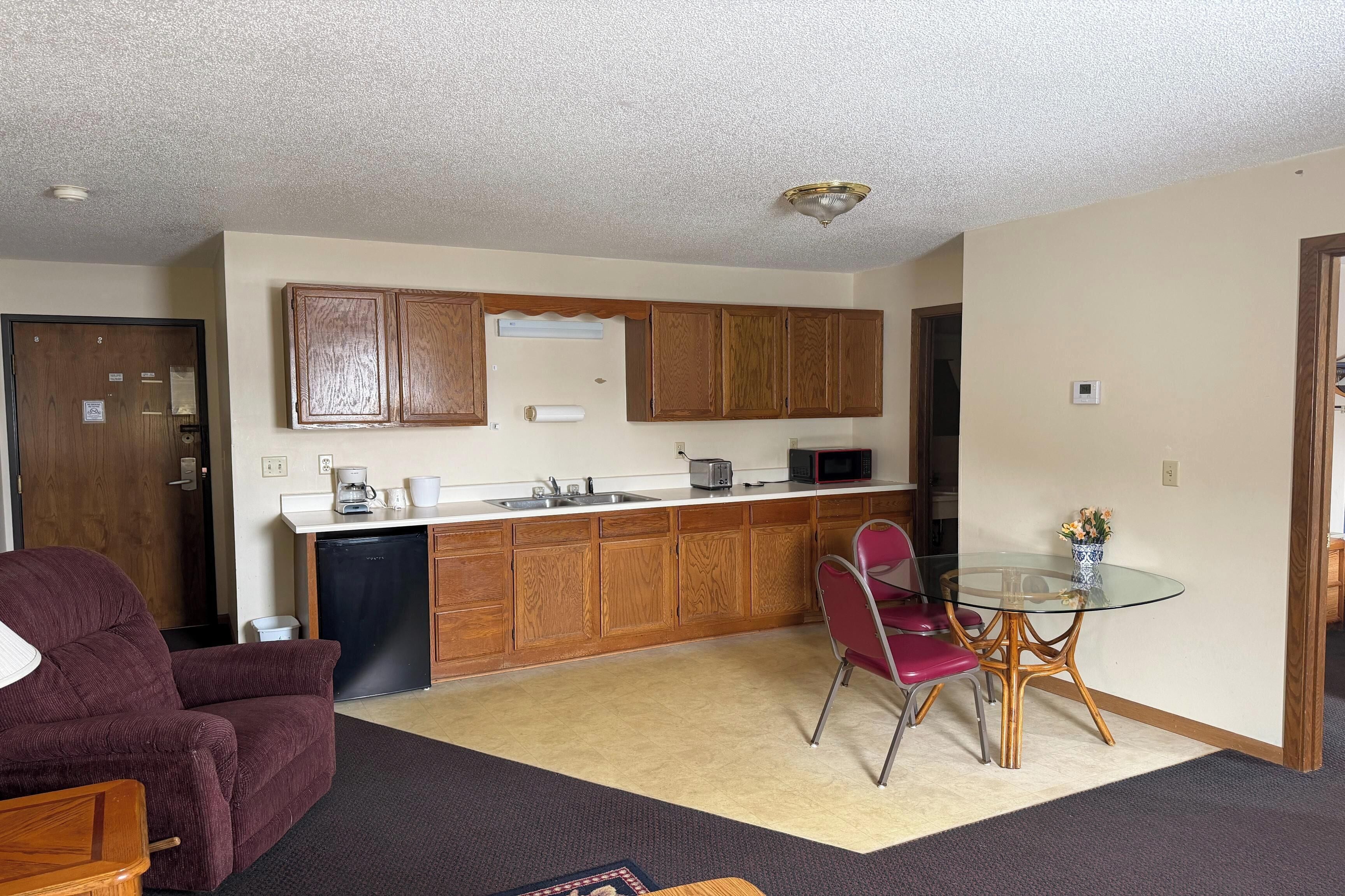 A compact living space with a kitchenette, a dining table with chairs, a sofa, and a carpeted floor.
