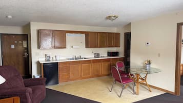 A compact living space with a kitchenette, a dining table with chairs, a sofa, and a carpeted floor.