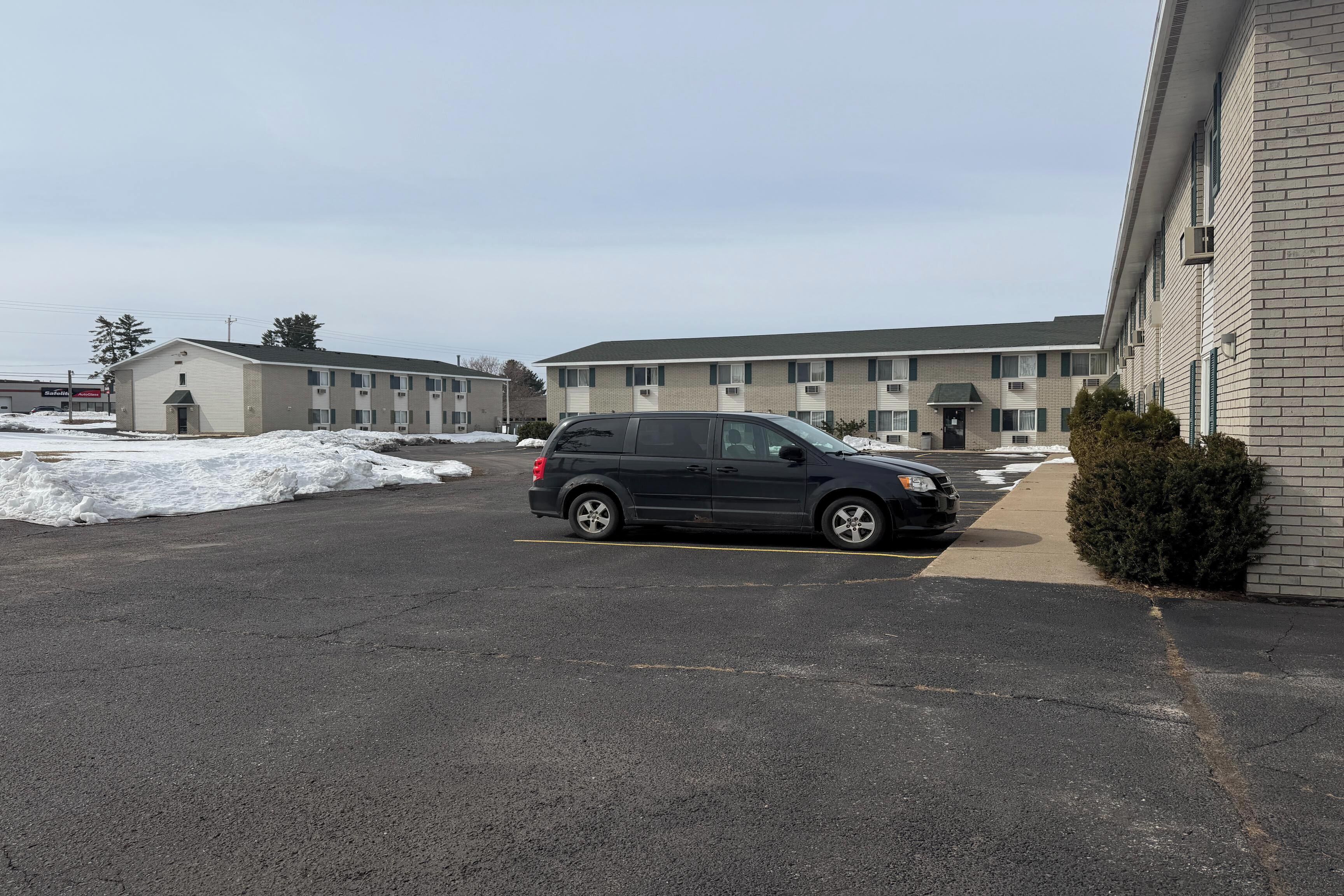 A parking lot with a black SUV, a building with multiple windows, and snow on the ground.