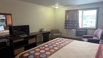 A hotel room with a bed, a desk with a TV, a chair, and a window with curtains.