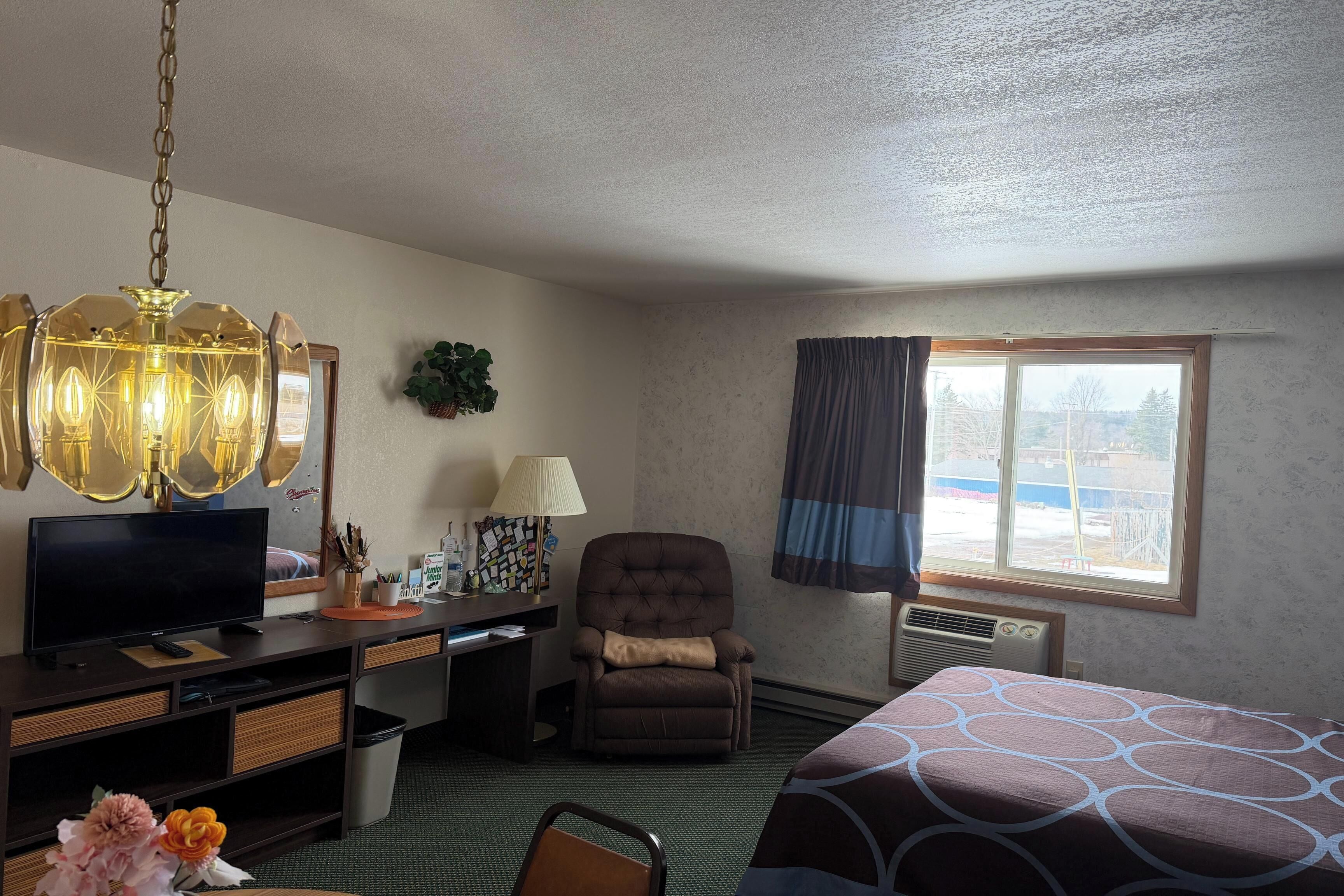 A hotel room with a bed, desk, chair, television, and a large window.