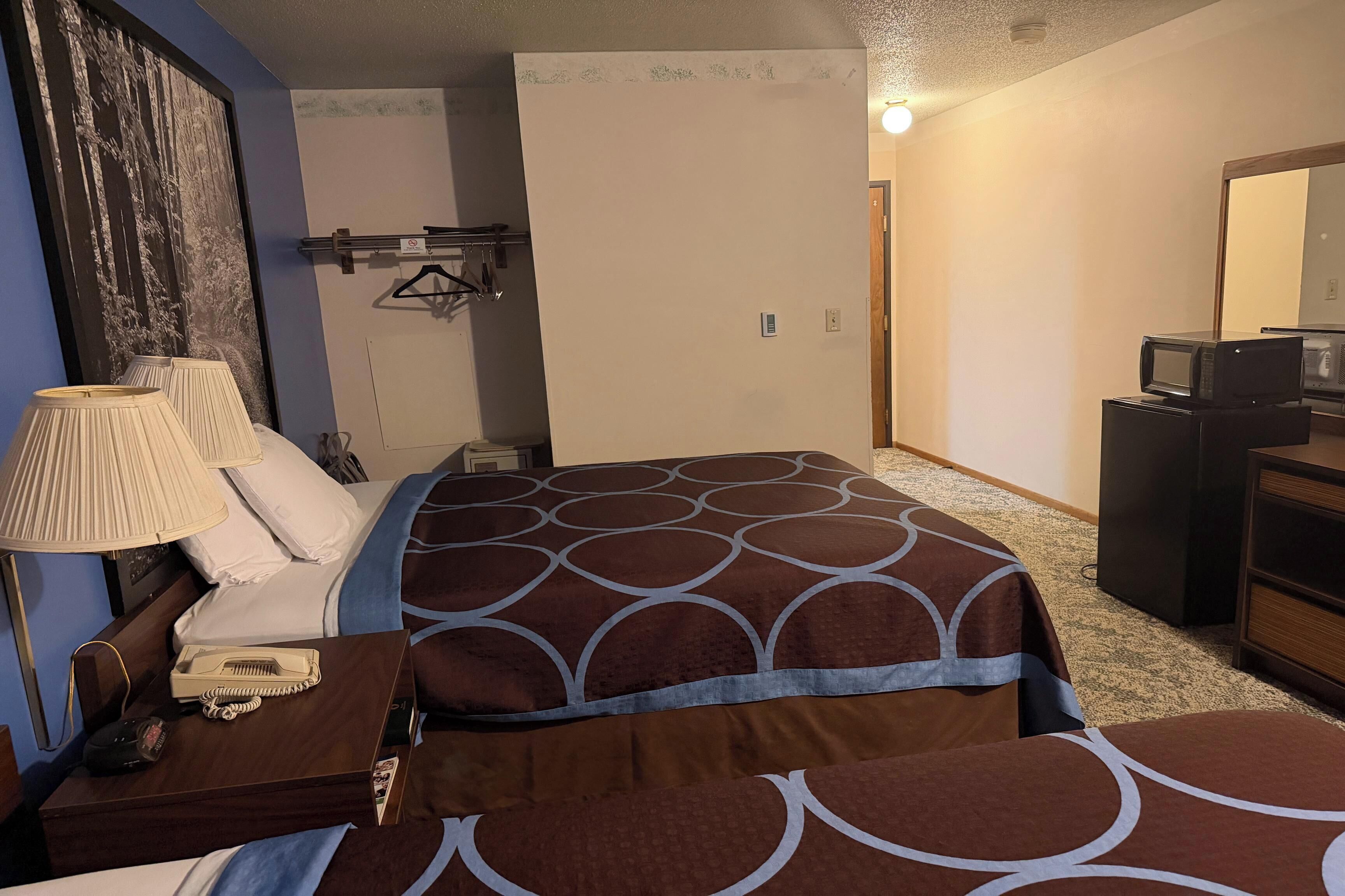 A hotel room with a bed, bedside table with lamp, dresser, and a mirror.
