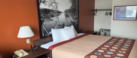 A hotel room with a bed, a nightstand with a lamp, a telephone, and a painting on the wall.