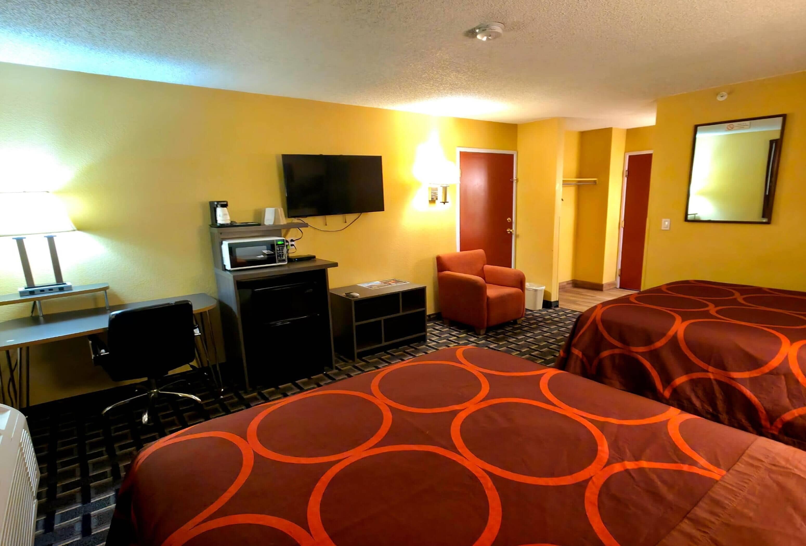 Une chambre d’hôtel équipée d’un bureau, d’une télévision, d’une chaise, de deux lits avec une literie à motifs circulaires, d’une lampe et d’un miroir.