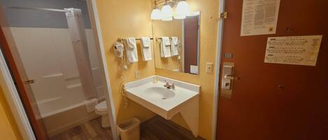 A bathroom with a white sink, mirror, and towel rack. There is a door with a fire evacuation plan on the wall.