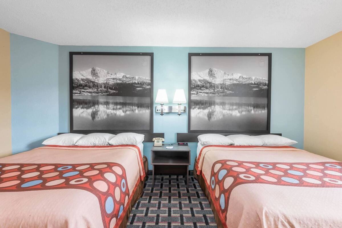 Habitació d'hotel amb dos llits, una nitòria amb una làmpada i dues fotografies emmarcades a la paret.