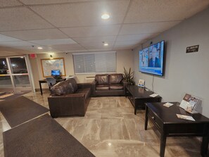 A lobby with a brown leather sofa, a TV on the wall, a desk with papers, and a map on the wall. - Super 8 by Wyndham Henderson North East Denver (Henderson)