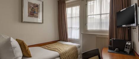 Quarto de hotel com uma cama, uma escrivaninha com computador, televisão, janela com cortinas e um quadro na parede.