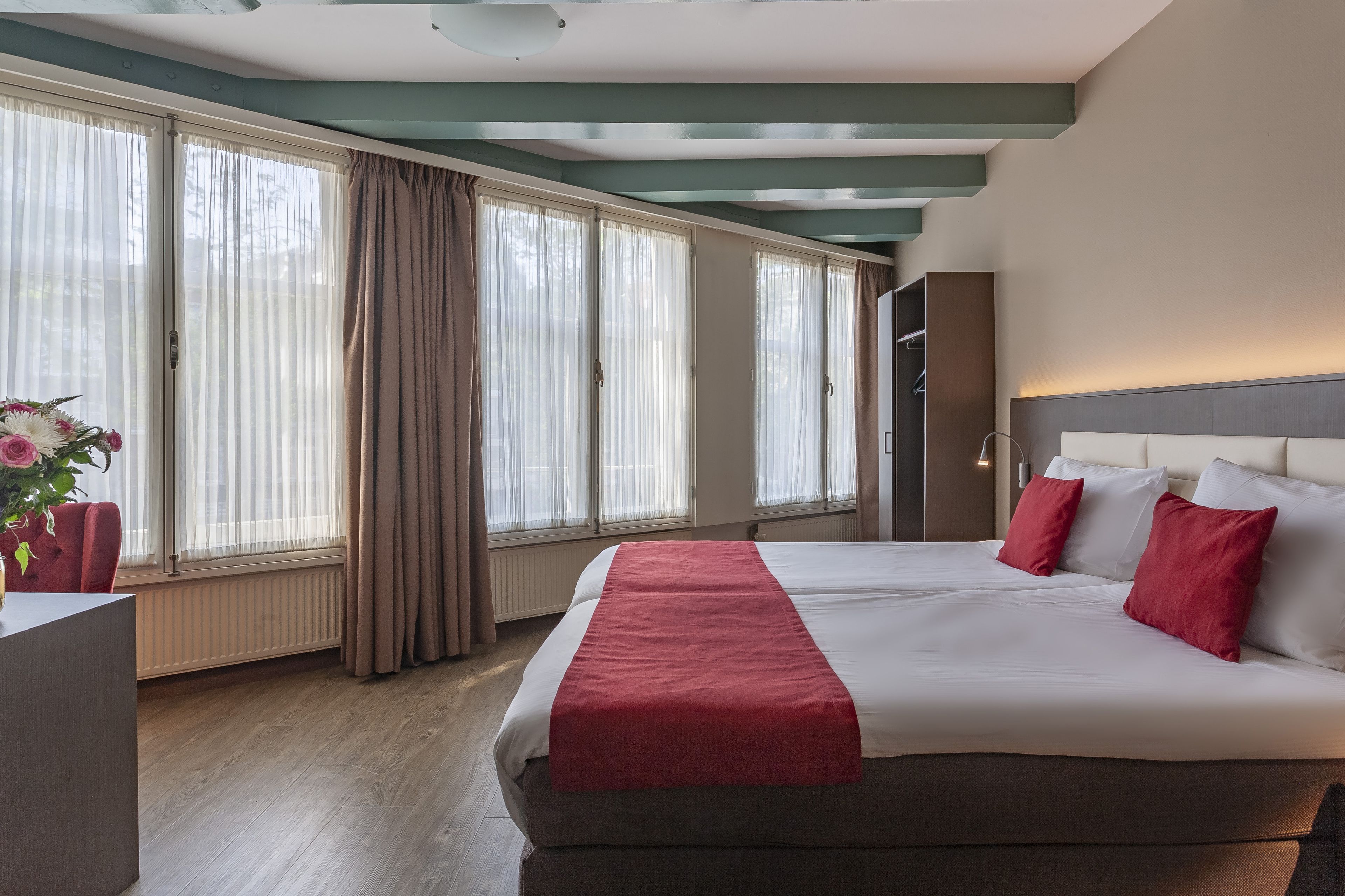A hotel room with a large bed, a desk, and a window with curtains.