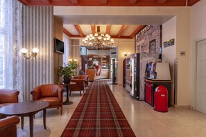 A hotel lobby with a plaid carpet, leather chairs, a reception desk, a TV, and a chandelier. - Hotel Avenue (Amsterdam)