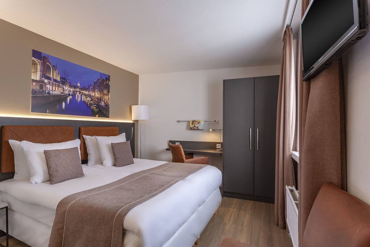 A hotel room with a large bed, a desk, a wardrobe, and a TV.