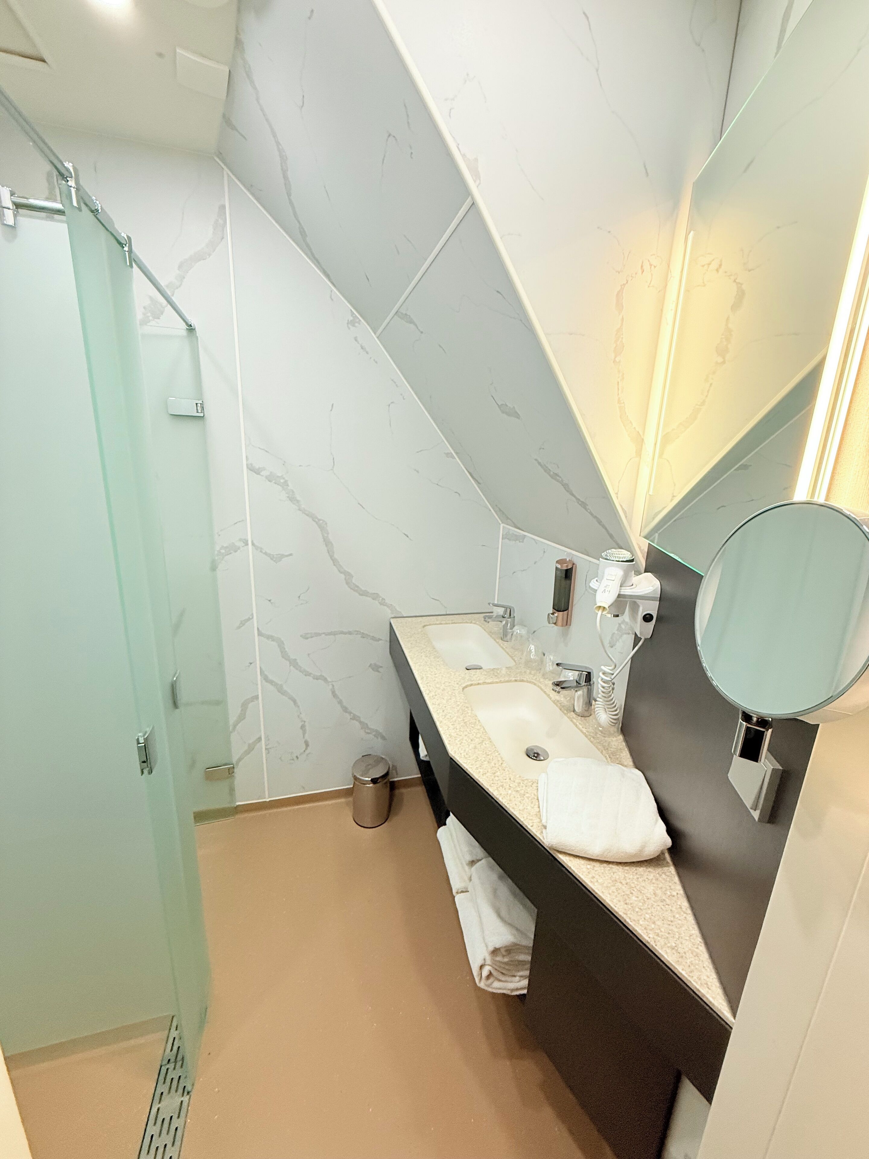 Un bagno moderno con box doccia in vetro, lavabo su piano beige e uno specchio grande.
