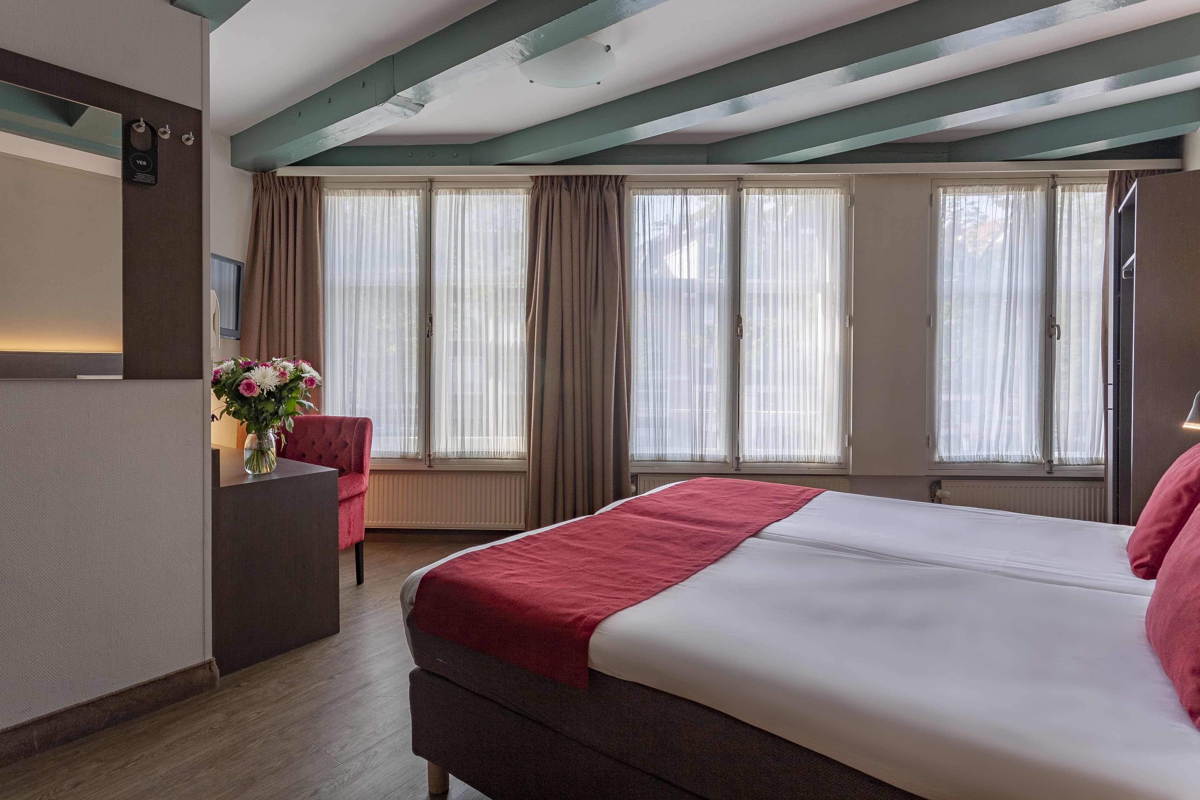 Habitación de hotel con cama, escritorio, silla y ventana con cortinas.