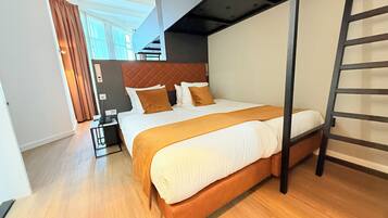Una habitación de hotel moderna con una cama grande, suelo de madera, cabecera y una escalera.