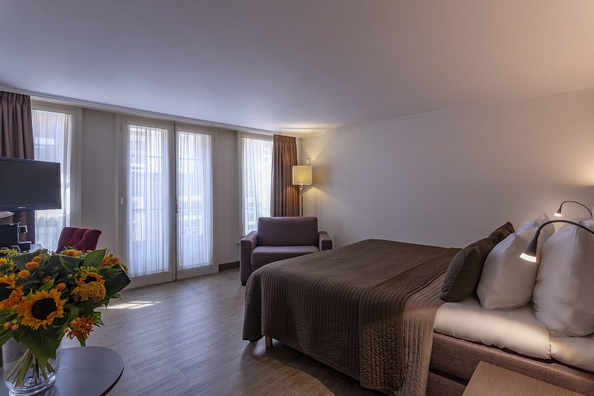 A hotel room with a bed, a chair, a TV, and a lamp.