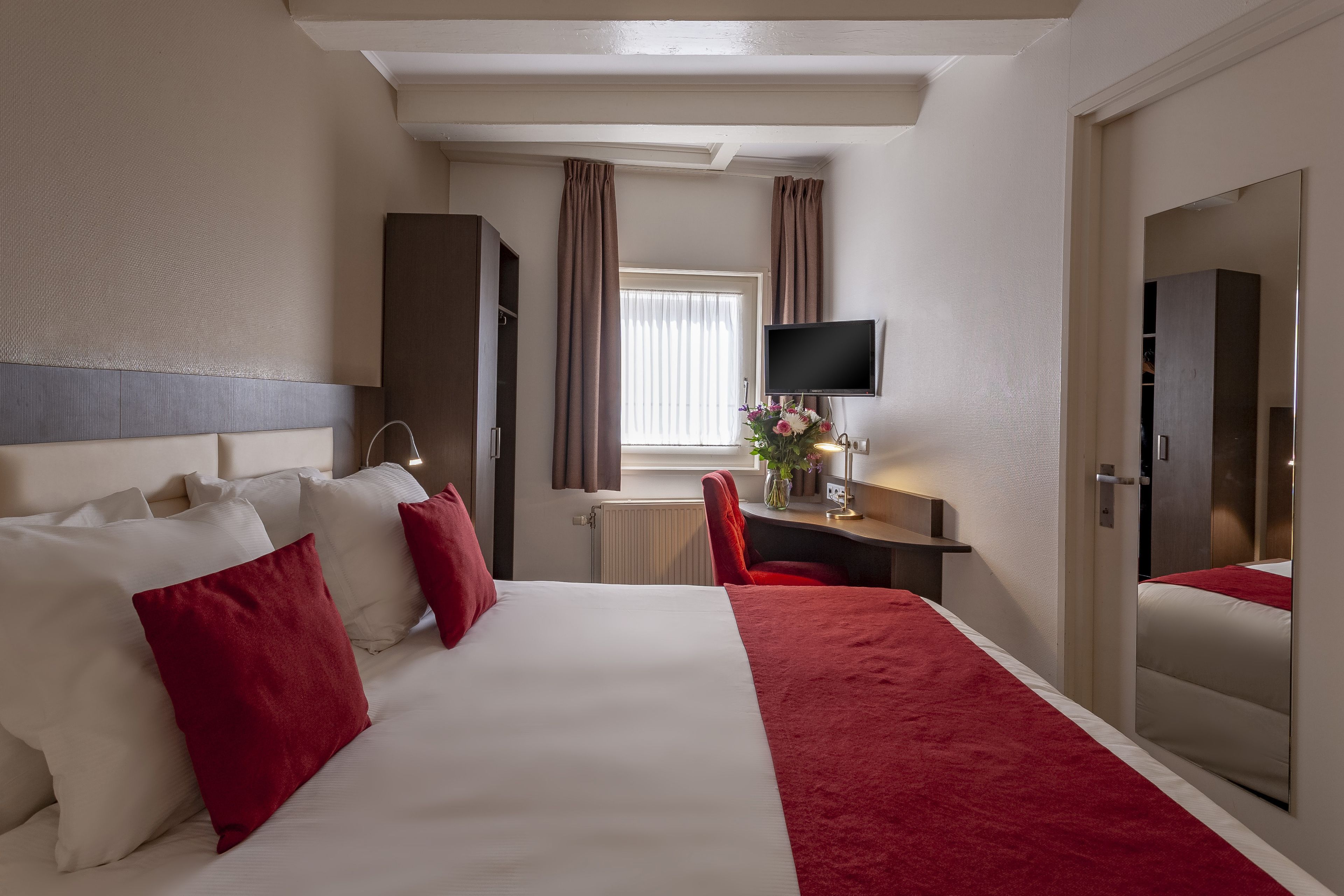 Una habitación de hotel con una cama grande, un escritorio, un televisor y un espejo.