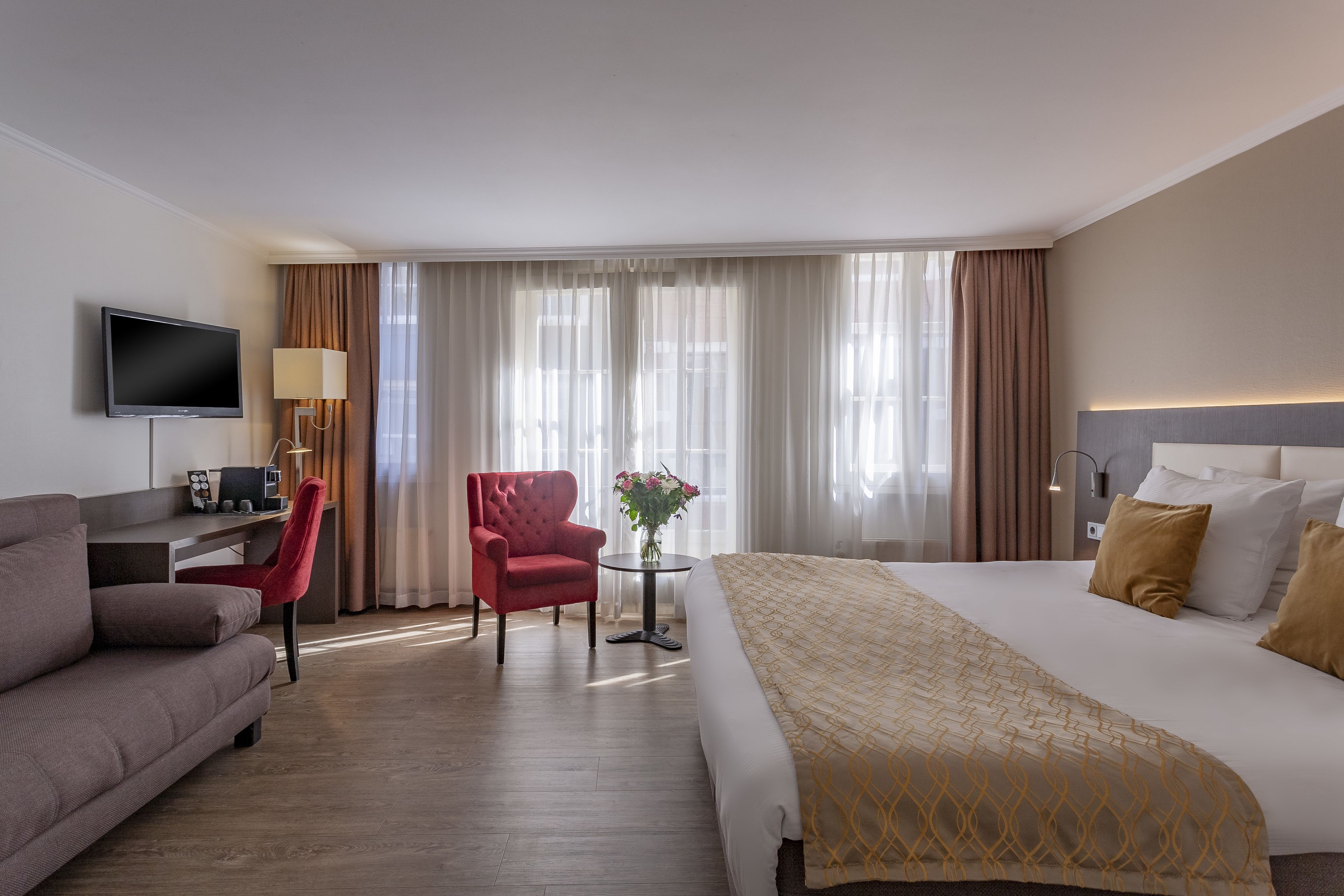 Une chambre d’hôtel avec un lit, un bureau, une chaise, une télévision et une fenêtre avec des rideaux.