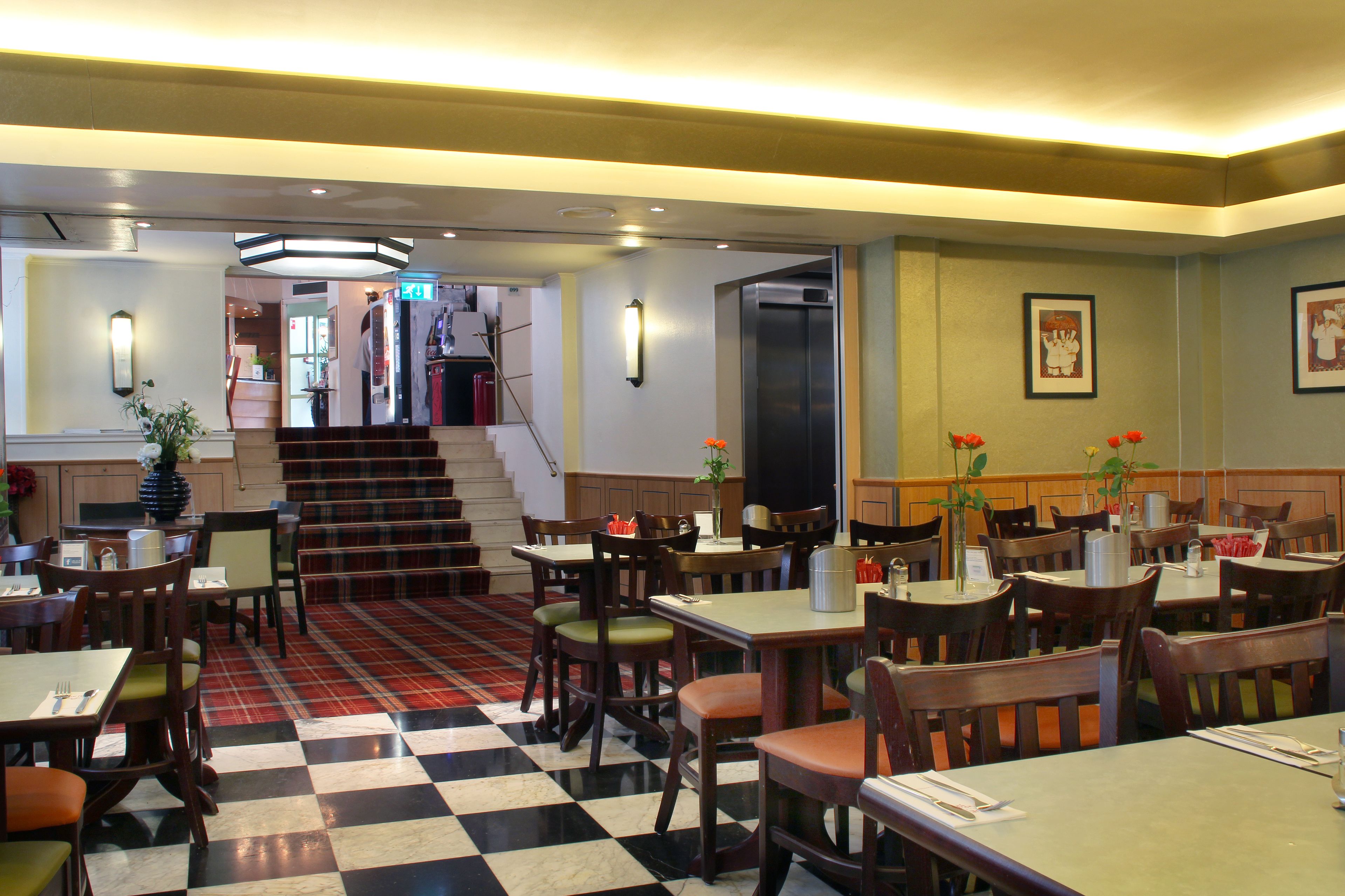 A restaurant with checkered flooring, wooden tables and chairs, and a staircase leading to an upper level.