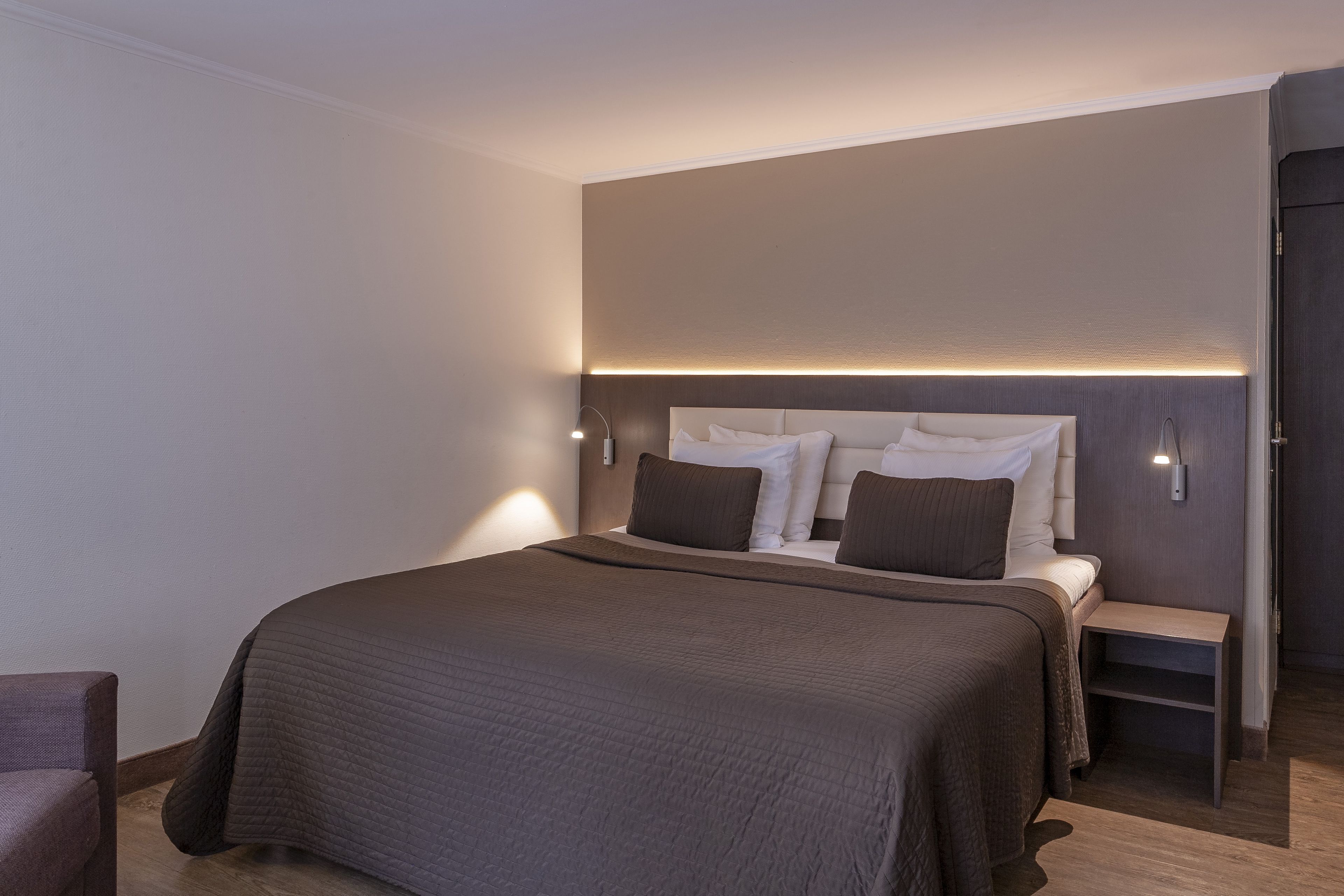 Una moderna camera d'albergo con un ampio letto, comodini e una testiera con illuminazione integrata.