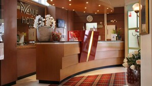 A hotel reception area with a curved reception desk, a clock, and a large mirror. - Hotel Avenue (Amsterdam)