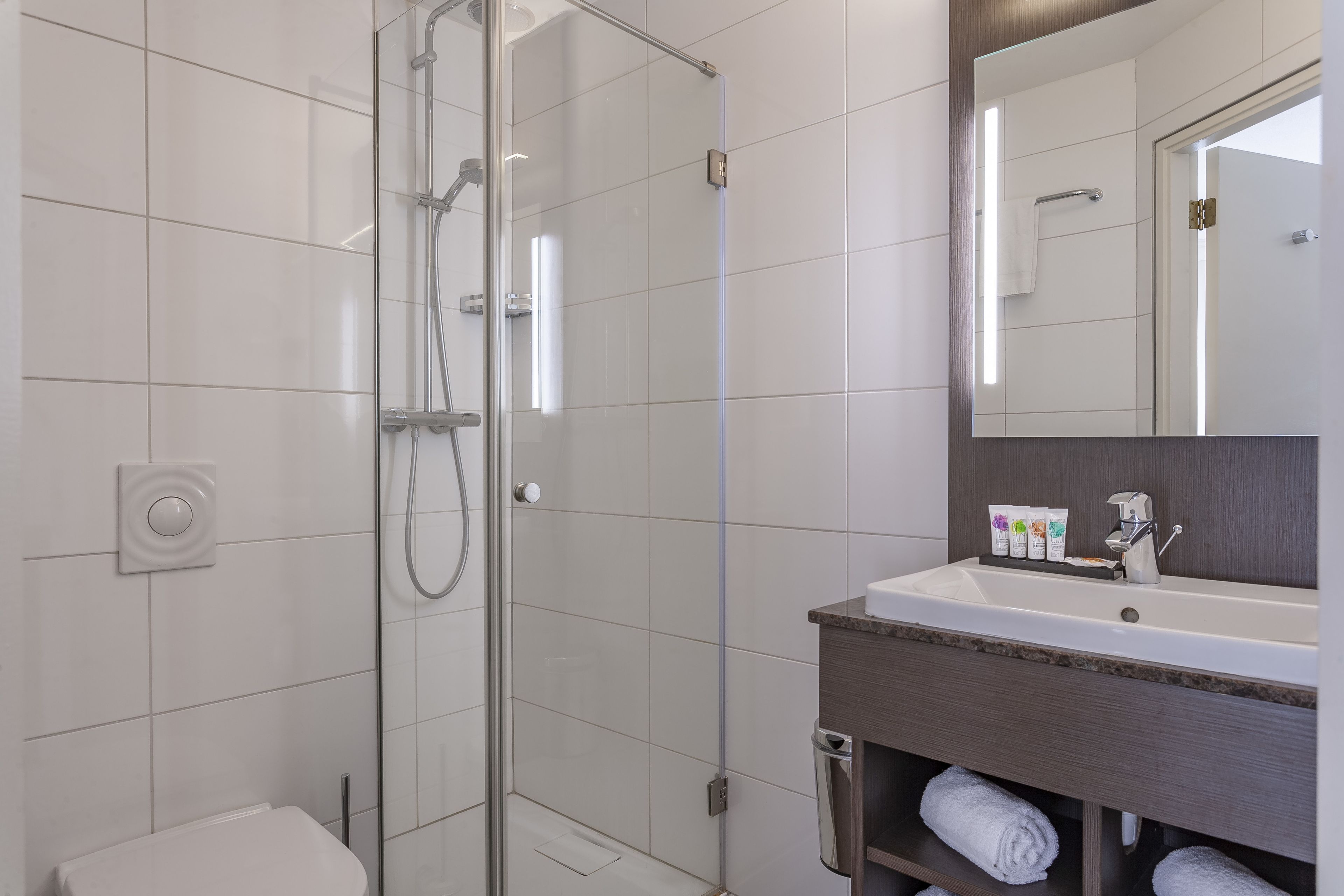 Un baño moderno con ducha envuelta en cristal, un lavabo blanco con encimera oscura y un espejo grande sobre el lavabo.