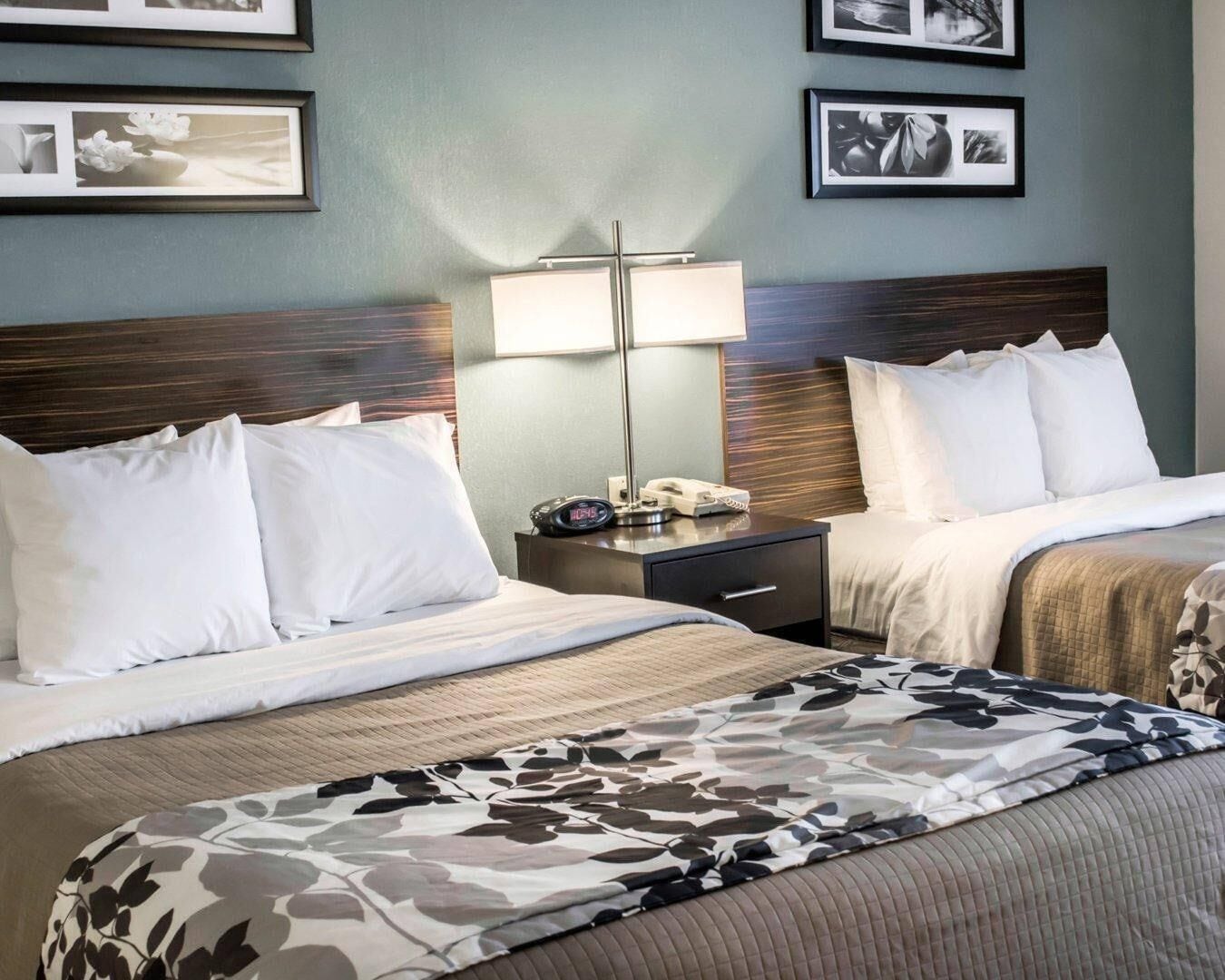 A hotel room with two beds, a nightstand with a lamp, and framed pictures on the wall.