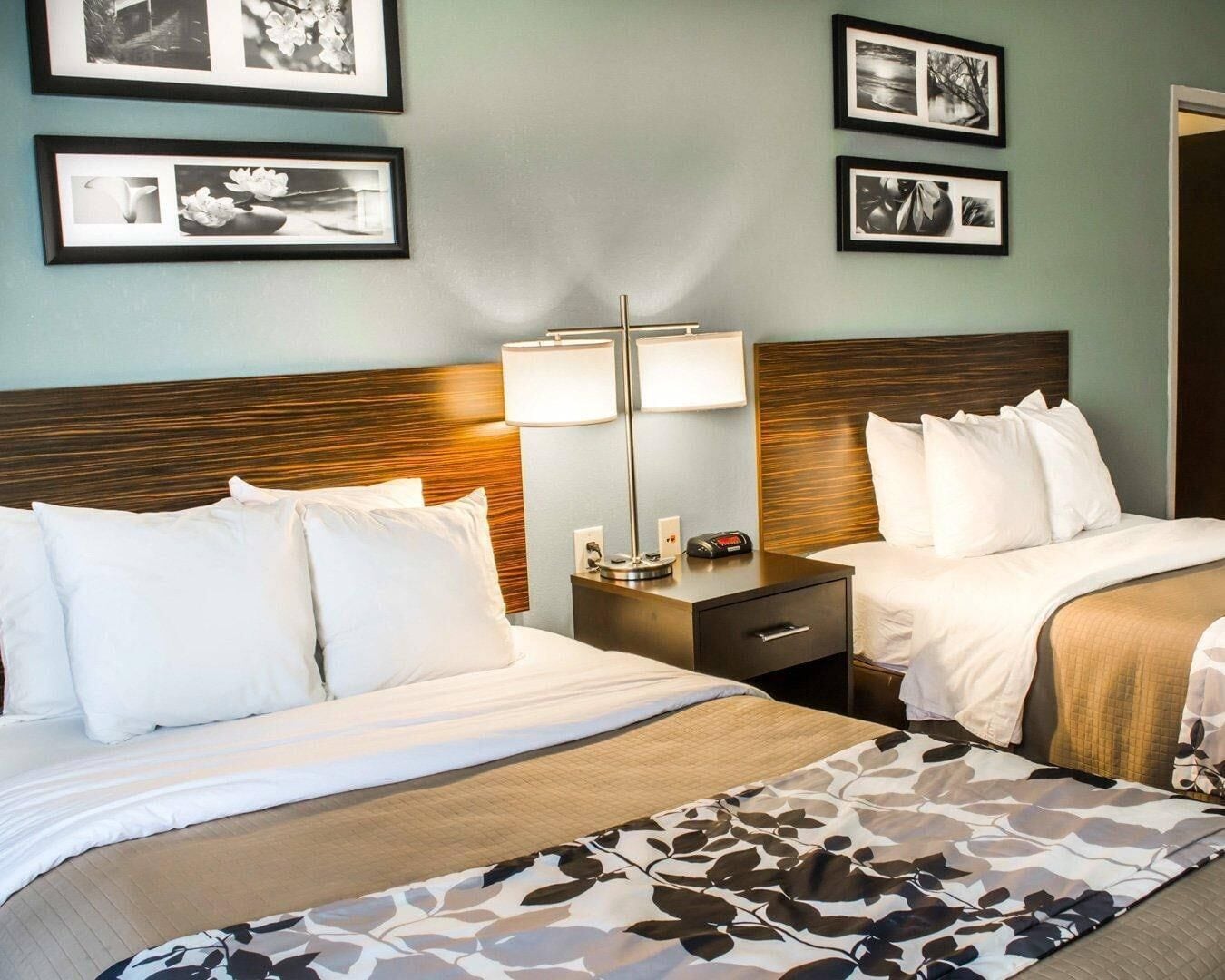 A hotel room with two beds, a nightstand with a lamp, and framed pictures on the wall.