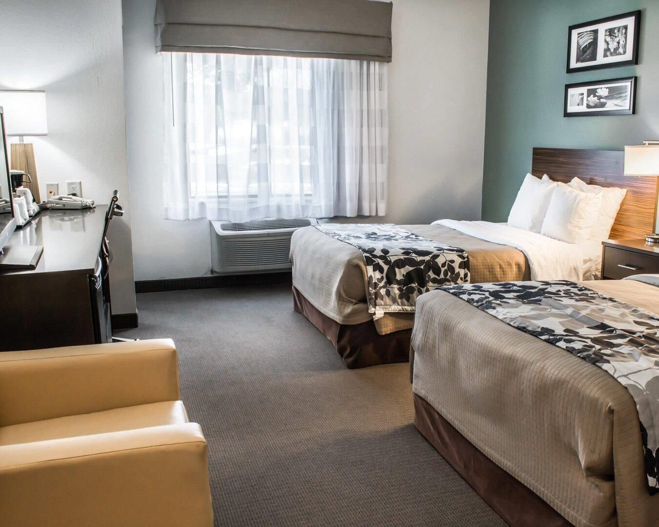 Une chambre d’hôtel avec deux lits, un bureau, une chaise, une fenêtre avec des rideaux et un mur orné de tableaux.