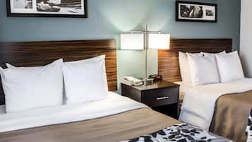 A hotel room with two beds, a nightstand with a lamp, and framed pictures on the wall.