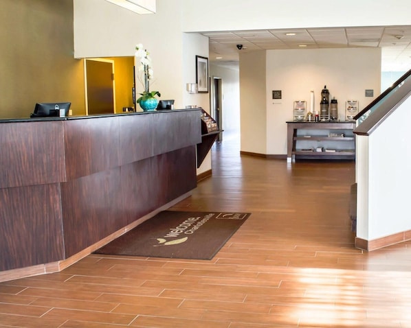 A reception area with a wooden reception desk, a welcome mat, a coffee station, and a staircase.
