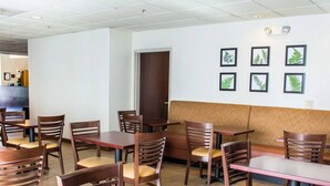 A restaurant interior with wooden tables and chairs, a seating area with a cushioned bench, and framed botanical prints on the wall. - Sleep Inn & Suites Monticello (Charlottesville)