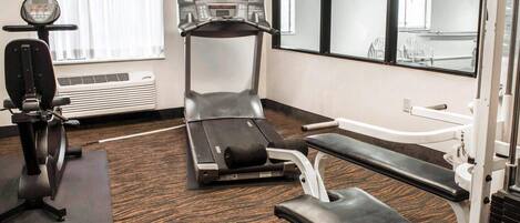 A gym with cardio machines, a bench, and a mirrored wall.