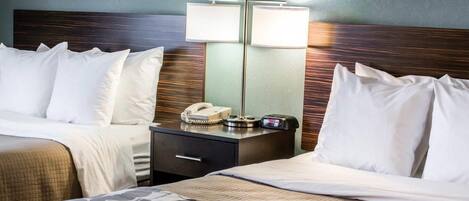 A hotel room with two beds, a bedside table with a lamp, a phone, and a clock.