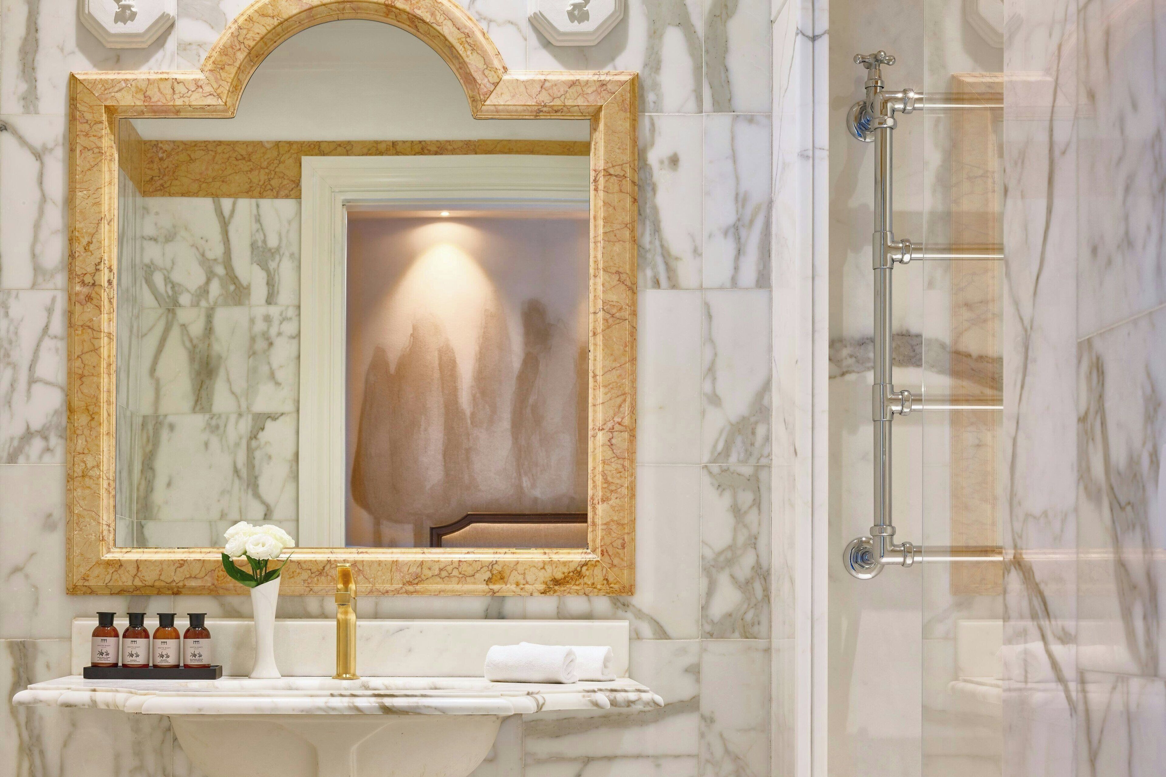 A bathroom with a marble vanity, a large mirror with a gold frame, and a shower area.