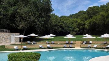 Une piscine entourée d’un mur de pierre et d’une végétation luxuriante, avec des chaises longues et des parasols à proximité.