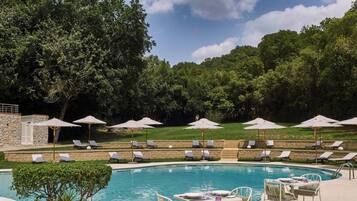A pool area with lounge chairs and umbrellas, surrounded by trees and a stone wall.