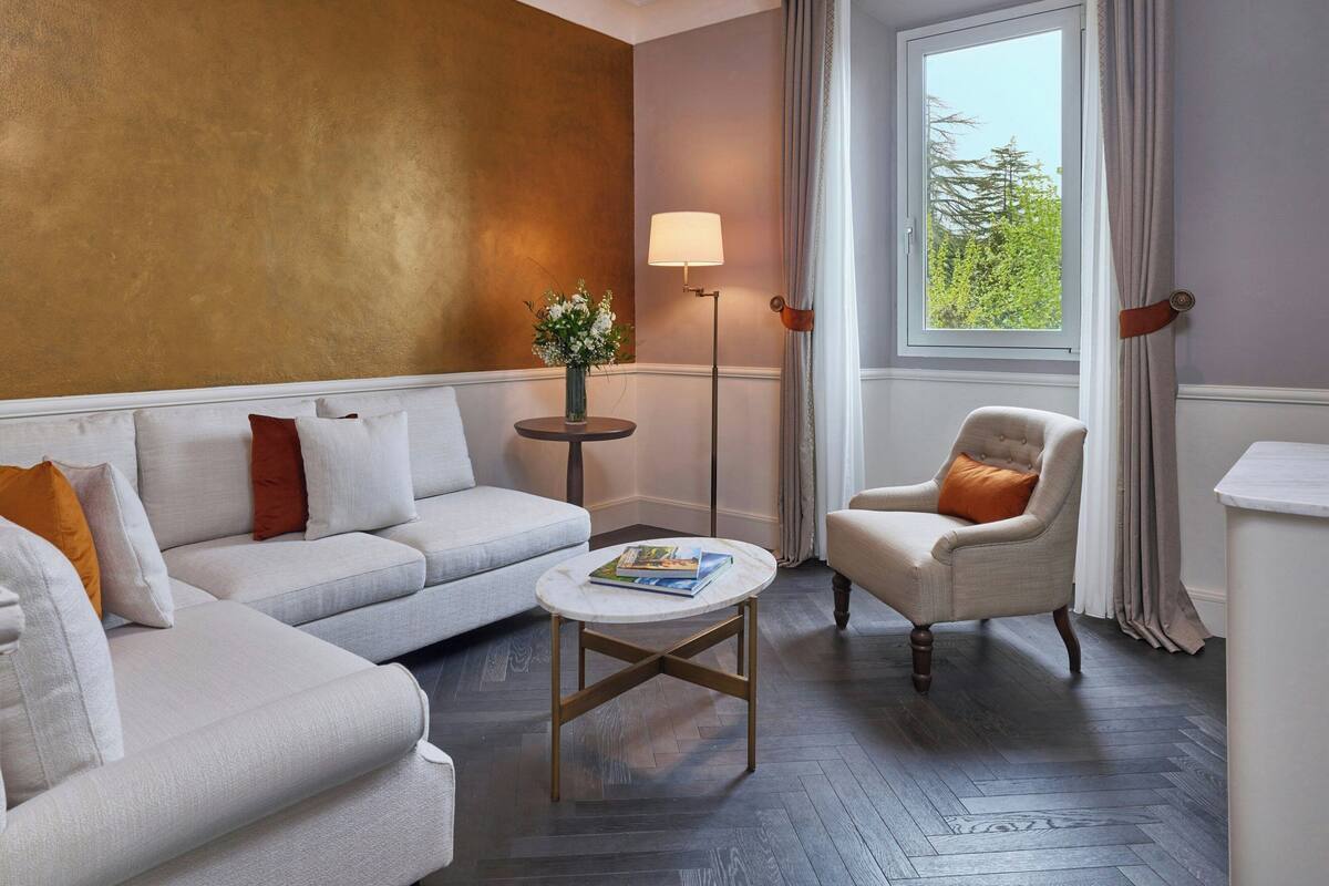 A living room with a sofa, armchair, round coffee table, floor lamp, and a window with curtains.