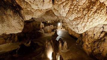Una cueva con estalactitas y estalagmitas, iluminación tenue y un estrecho pasadizo.